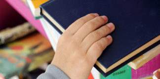 Kid's Hand Taking Book from a Shelf in Public Library.