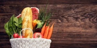 White basket full of groceries and vegetables on wood background