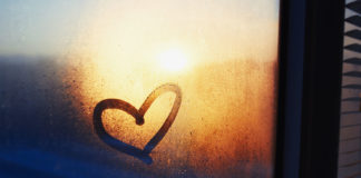 Heart drawn on a misty window and sunset on the background