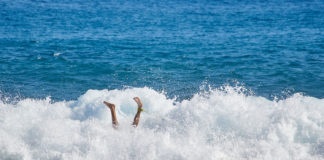 Surfer in wave wipes out and falls off surf board.